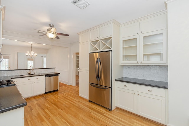 kitchen featuring visible vents, a sink, stainless steel appliances, light wood-style floors, and decorative backsplash