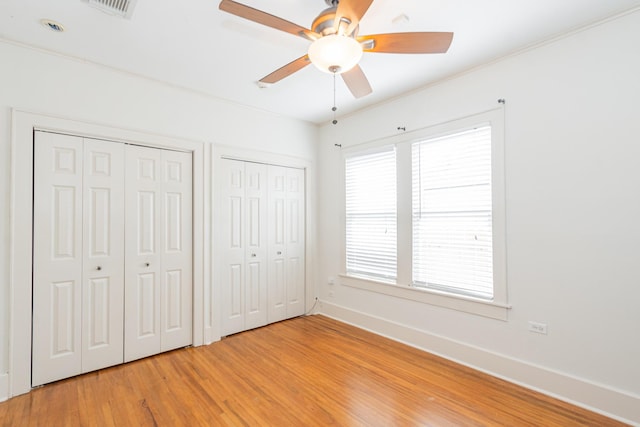 unfurnished bedroom with light wood finished floors, visible vents, multiple windows, and two closets