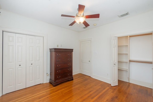 unfurnished bedroom with visible vents, two closets, baseboards, and wood finished floors