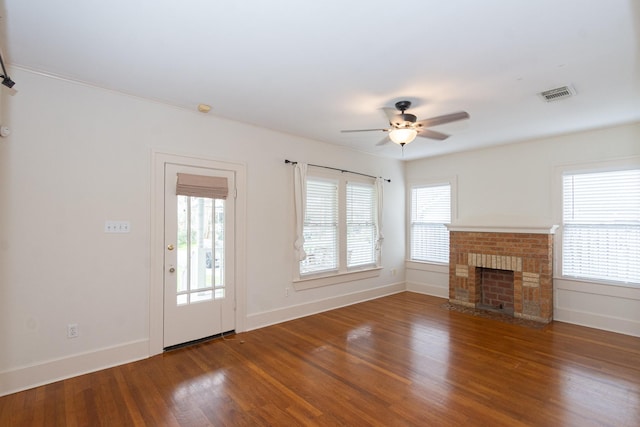 unfurnished living room featuring visible vents, a healthy amount of sunlight, a brick fireplace, and wood finished floors