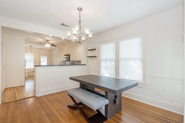 dining room featuring light wood finished floors, visible vents, ceiling fan with notable chandelier, and baseboards