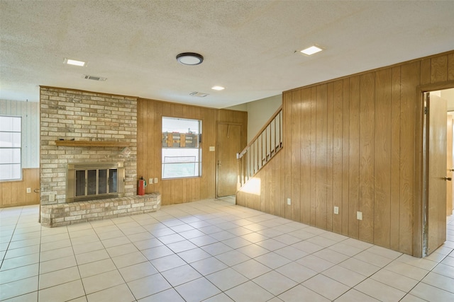 unfurnished living room with wooden walls, plenty of natural light, a fireplace, and visible vents