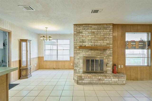 unfurnished living room with a textured ceiling, tile patterned floors, visible vents, and wainscoting