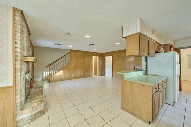 kitchen with open floor plan, freestanding refrigerator, light countertops, light tile patterned floors, and a brick fireplace