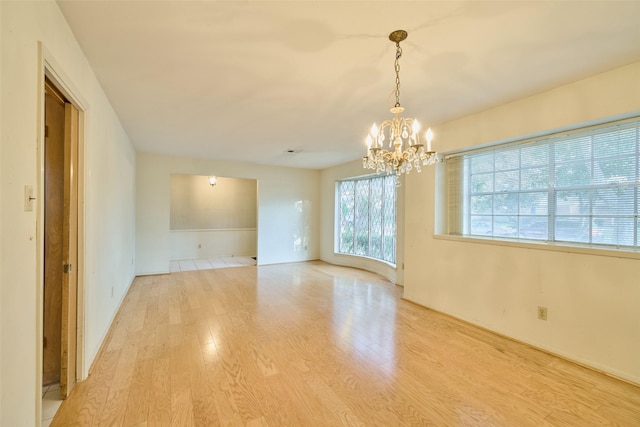 spare room featuring a notable chandelier and light wood-type flooring