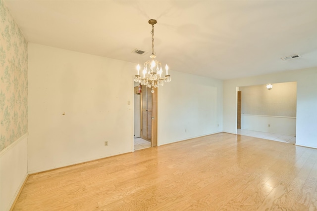 spare room with a chandelier, visible vents, light wood-style flooring, and wallpapered walls