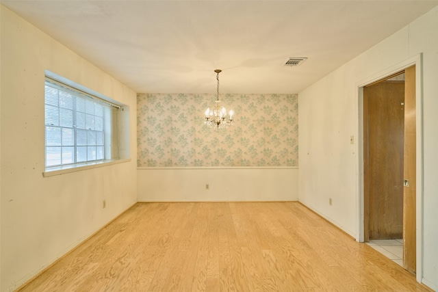 unfurnished room with visible vents, a notable chandelier, wood finished floors, wainscoting, and wallpapered walls