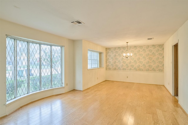 spare room with visible vents, wallpapered walls, wainscoting, wood finished floors, and a notable chandelier