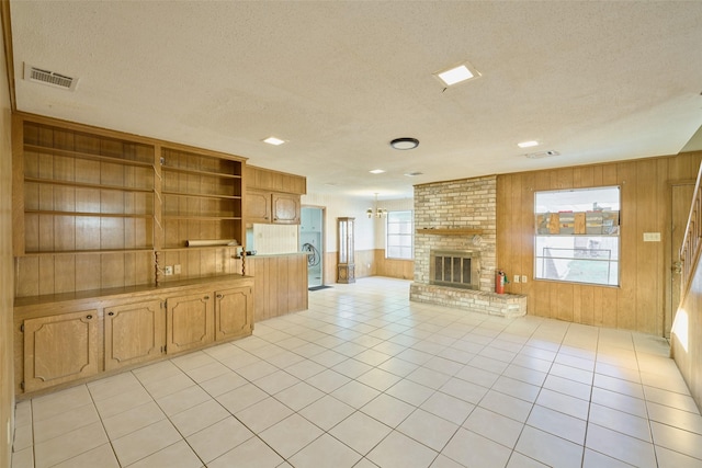 unfurnished living room with wooden walls, light tile patterned floors, visible vents, a textured ceiling, and a brick fireplace