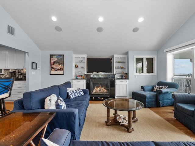 living room featuring visible vents, a glass covered fireplace, wood finished floors, recessed lighting, and lofted ceiling