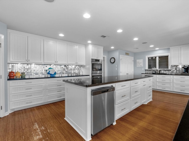 kitchen featuring stainless steel appliances, dark countertops, wood finished floors, and white cabinetry