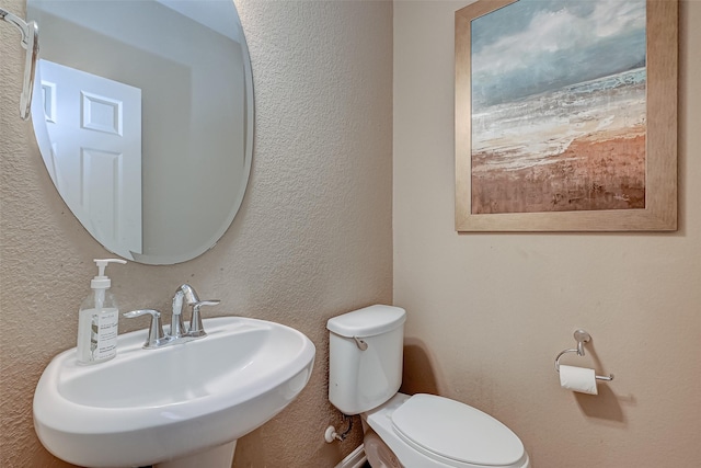 bathroom featuring a sink, toilet, and a textured wall