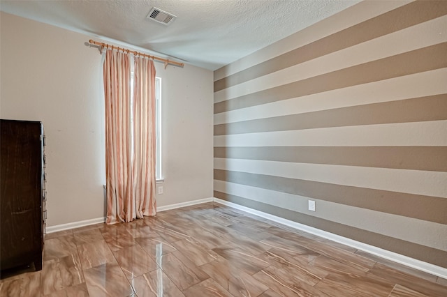 unfurnished room with visible vents, baseboards, a textured ceiling, and plenty of natural light