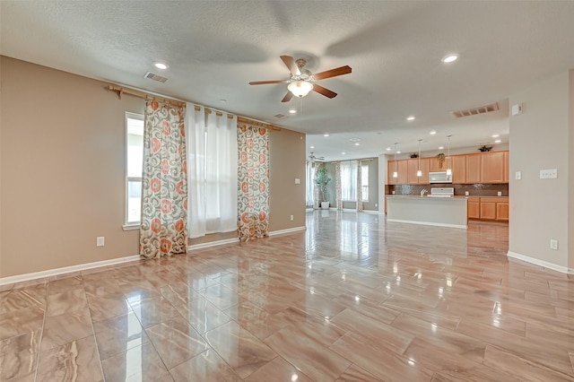 unfurnished living room with visible vents, baseboards, a textured ceiling, and ceiling fan