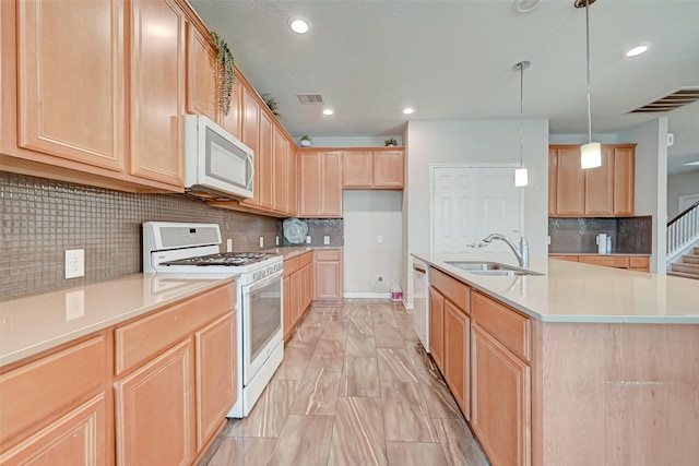 kitchen with white appliances, light brown cabinets, visible vents, a center island with sink, and a sink