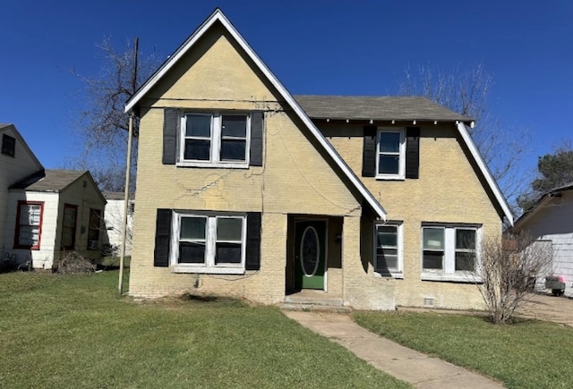 tudor-style house featuring brick siding and a front yard