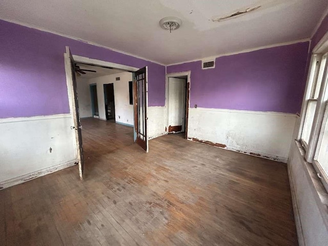 spare room with a wainscoted wall, crown molding, wood finished floors, and visible vents