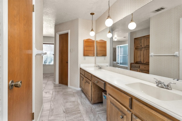 bathroom featuring a sink, a textured ceiling, double vanity, and wallpapered walls