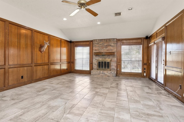 unfurnished living room with visible vents, wood walls, a fireplace, lofted ceiling, and ceiling fan