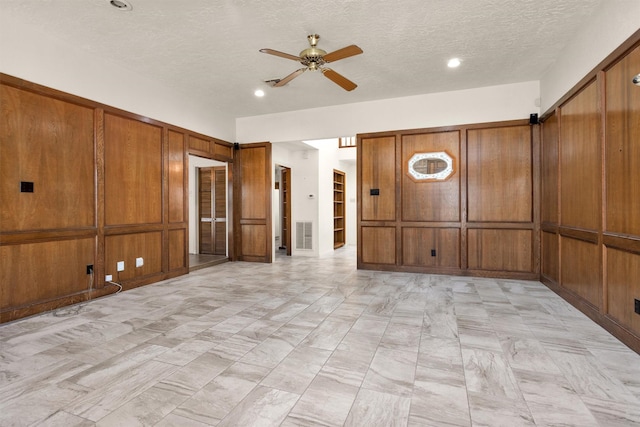 spare room featuring visible vents, wood walls, a textured ceiling, and ceiling fan