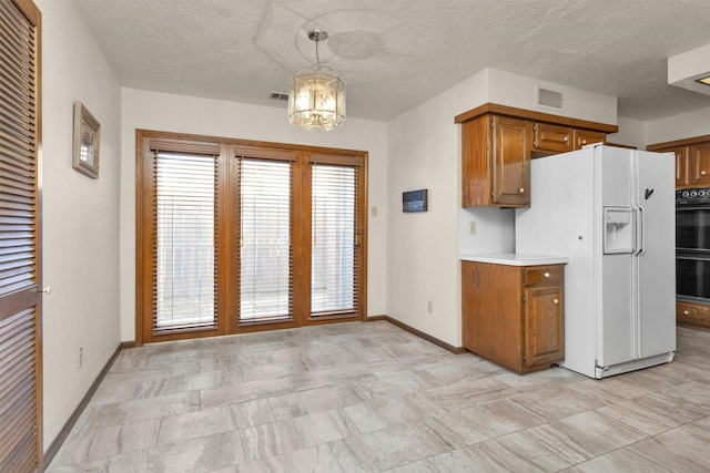 kitchen with brown cabinetry, visible vents, light countertops, and white fridge with ice dispenser