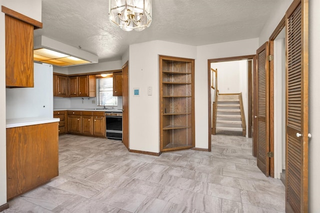 kitchen featuring baseboards, light countertops, black dishwasher, brown cabinets, and a textured ceiling