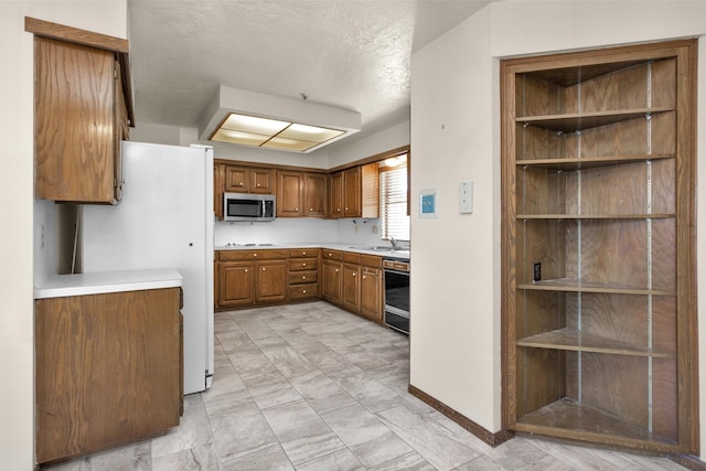 kitchen with stainless steel microwave, dishwasher, freestanding refrigerator, brown cabinetry, and a sink