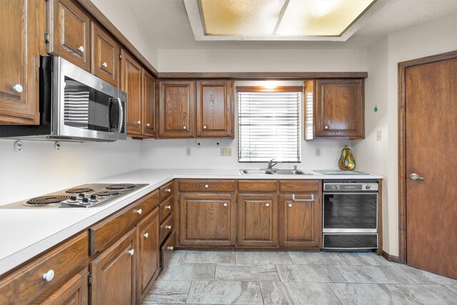 kitchen featuring brown cabinets, appliances with stainless steel finishes, light countertops, and a sink