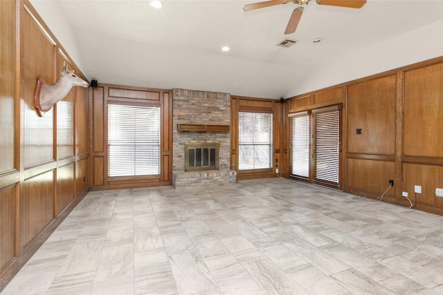 unfurnished living room with visible vents, wooden walls, a brick fireplace, and vaulted ceiling