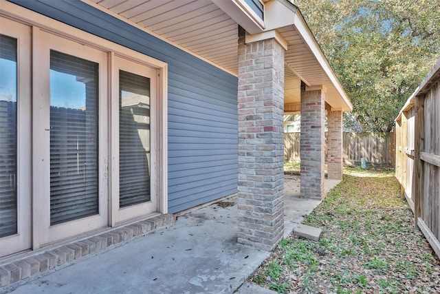 view of exterior entry with a patio, fence, brick siding, and french doors