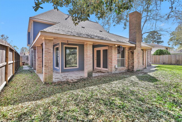 back of property with brick siding, a shingled roof, a chimney, a yard, and a fenced backyard