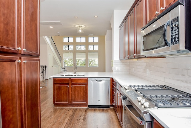 kitchen with a peninsula, light wood-style flooring, a sink, stainless steel appliances, and tasteful backsplash