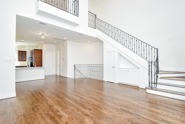 unfurnished living room featuring wood finished floors, visible vents, baseboards, stairs, and a towering ceiling