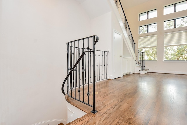 stairway with baseboards, a high ceiling, and wood finished floors