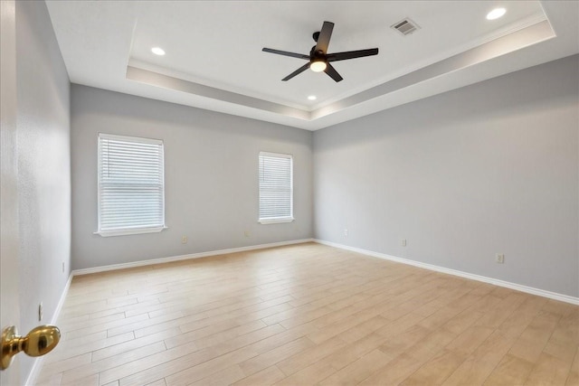 empty room with a tray ceiling, plenty of natural light, light wood-style floors, and visible vents