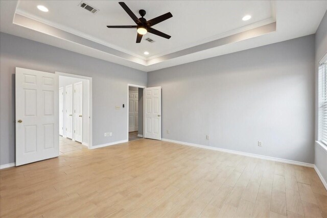 empty room with visible vents, light wood-style flooring, a raised ceiling, and baseboards