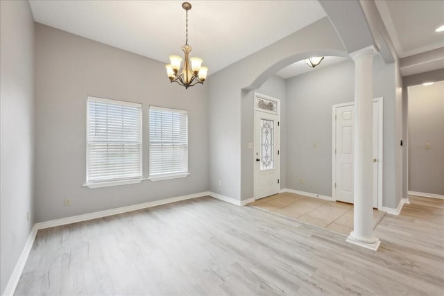 interior space with light wood finished floors, baseboards, a chandelier, decorative columns, and arched walkways