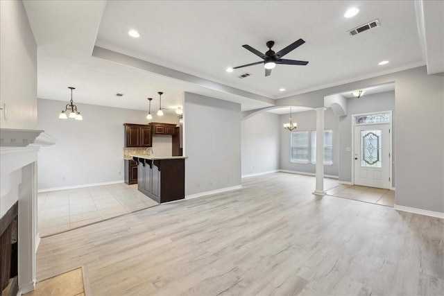 unfurnished living room with visible vents, light wood-type flooring, ceiling fan with notable chandelier, a fireplace, and arched walkways