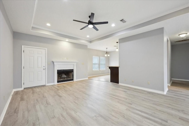 unfurnished living room with visible vents, baseboards, a fireplace, light wood finished floors, and a raised ceiling