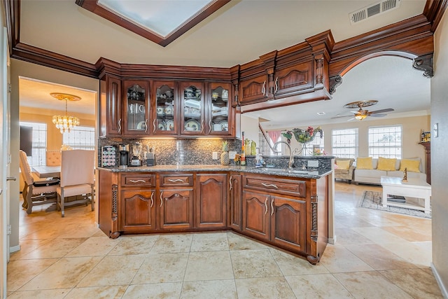 kitchen with visible vents, backsplash, dark stone counters, ornamental molding, and a peninsula