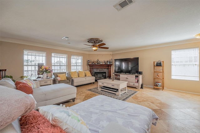 living area featuring a glass covered fireplace, visible vents, ornamental molding, and a ceiling fan