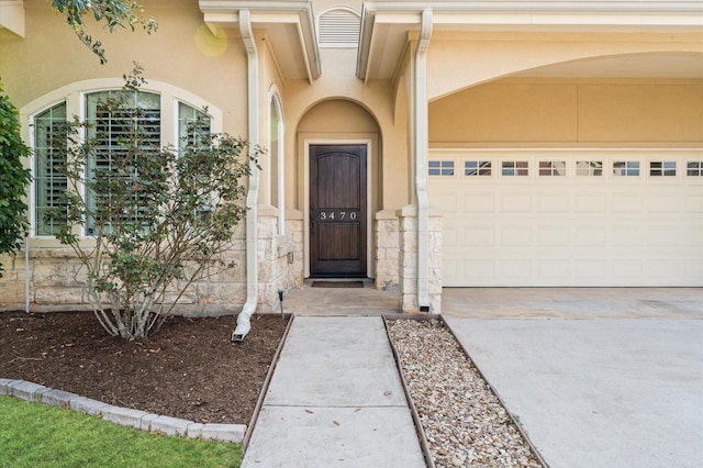 view of exterior entry featuring stone siding, stucco siding, concrete driveway, and a garage