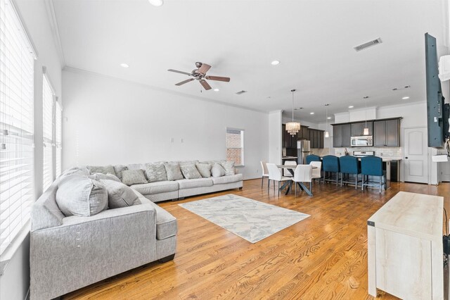 living room with visible vents, ceiling fan with notable chandelier, recessed lighting, light wood-style floors, and crown molding