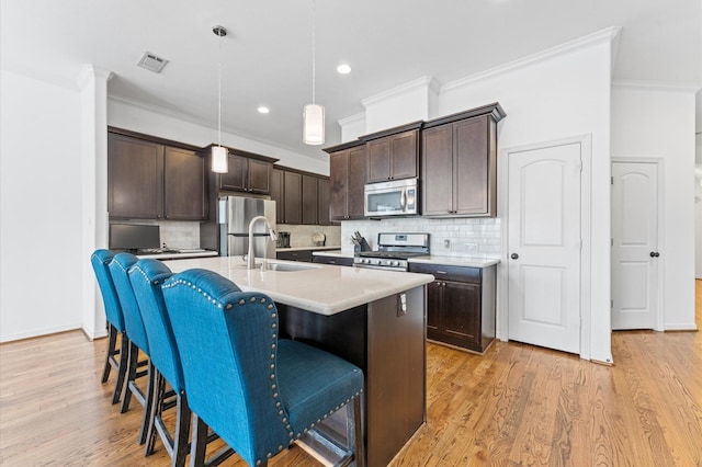 kitchen with dark brown cabinets, appliances with stainless steel finishes, a kitchen island with sink, and light wood finished floors