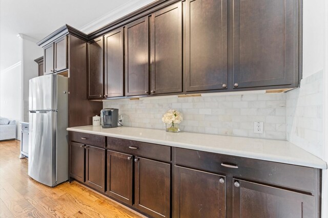 kitchen with light wood finished floors, freestanding refrigerator, decorative backsplash, light countertops, and dark brown cabinets