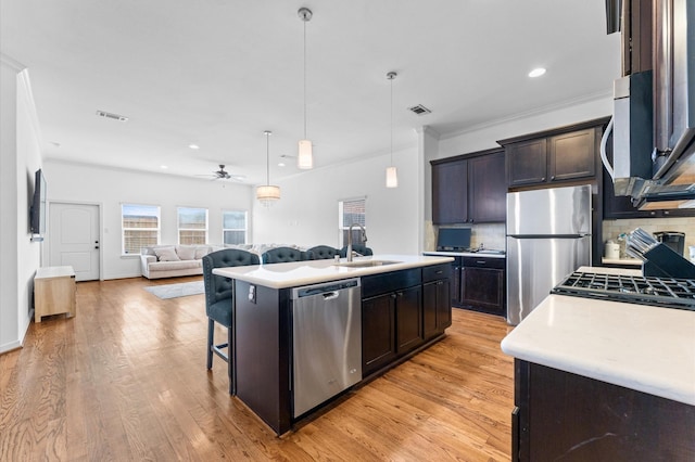 kitchen with light wood-style flooring, a sink, decorative backsplash, light countertops, and appliances with stainless steel finishes