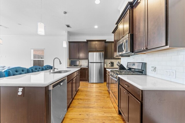 kitchen with open floor plan, light countertops, appliances with stainless steel finishes, light wood-style floors, and a sink