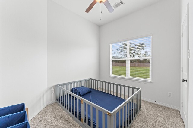 carpeted bedroom featuring a ceiling fan, a nursery area, baseboards, and visible vents