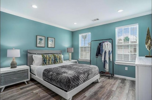 bedroom featuring multiple windows, wood finished floors, visible vents, and ornamental molding