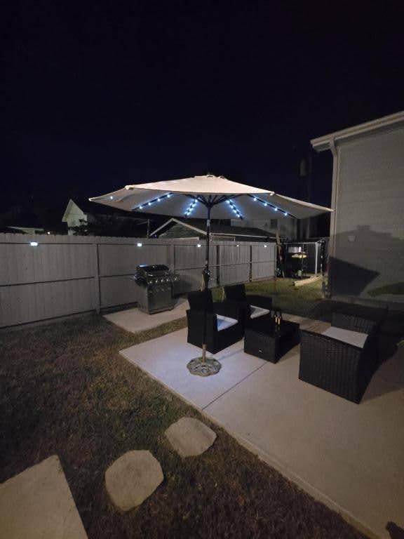 patio at night with an outdoor living space with a fire pit and a fenced backyard